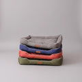 Stack of four pet beds in gray, blue, red, and green on a wooden floor.