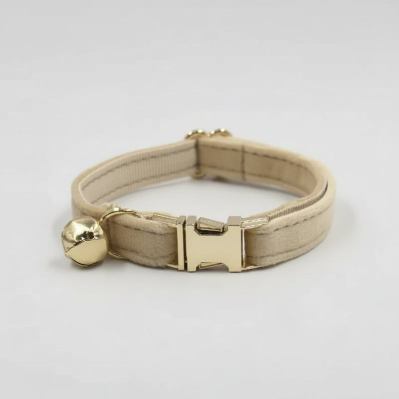 Cream velvet cat collar with polished gold hardware and bell styled in warm editorial lighting for modern luxury pets.