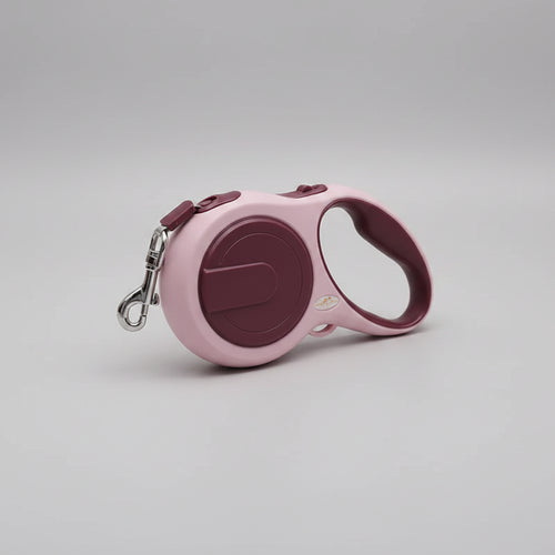 Pink and purple retractable dog leash on a white surface with a soft fabric background