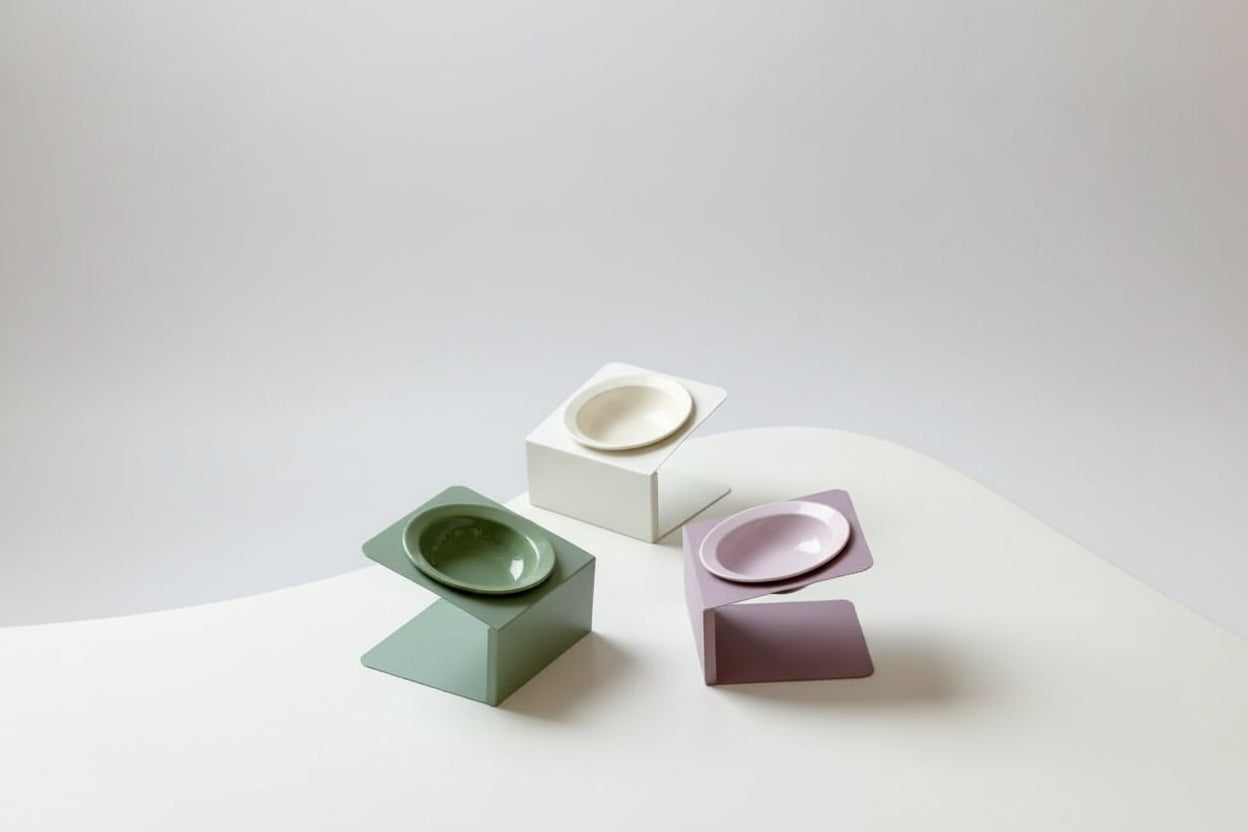 Three ceramic bowls in different colors on geometric stands against a neutral background