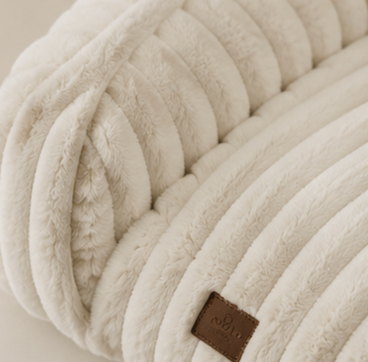 Close-up of a textured bone white pet bed with a brand label on a neutral background