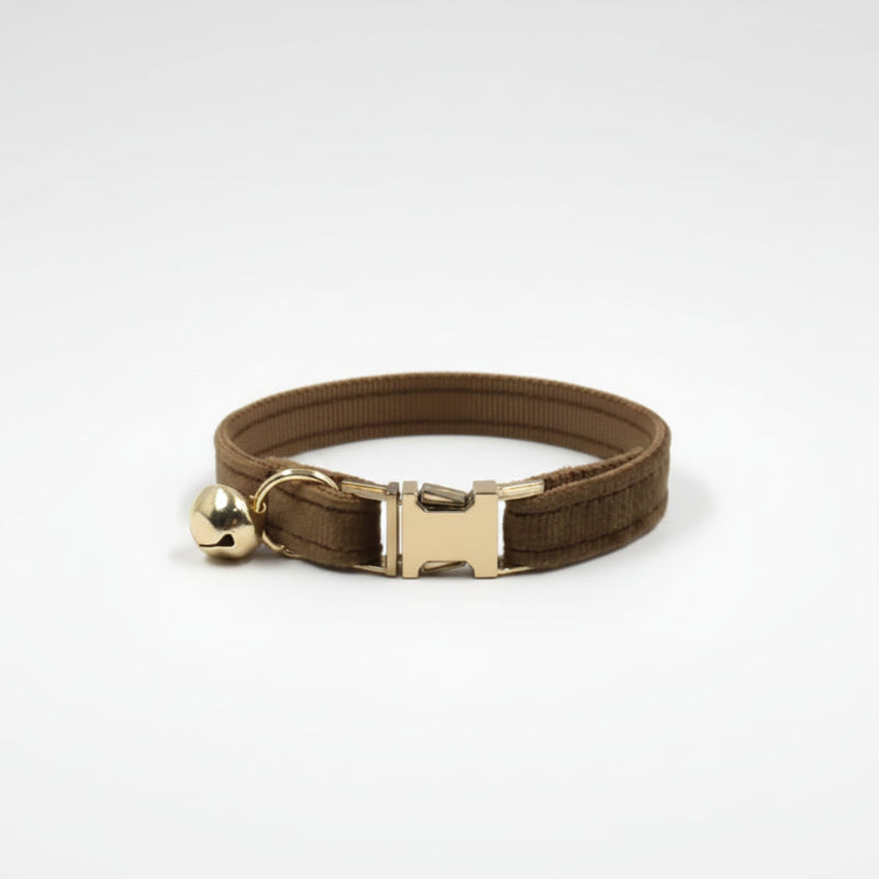 Brown velvet cat collar with polished gold hardware and bell styled in warm editorial lighting for modern luxury pets.